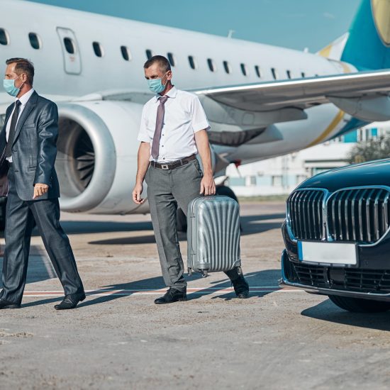 Chauffer helping boss with luggage to plane Elegant businessman with assistant with suitcase is coming by car to airport runway for flying during quarantine